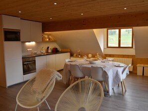 Ein gemütlicher Essbereich mit Tisch für vier Personen, eine Küche mit modernen Geräten und ein großes Fenster, das für natürliches Licht sorgt.