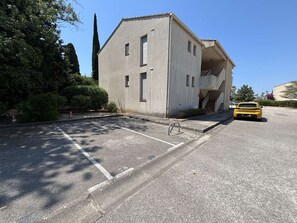 A building with a parking lot, a yellow car, and a staircase leading to an upper level. - Cozy apartment with parking, sea view - 4 guests (Sanary-sur-Mer)
