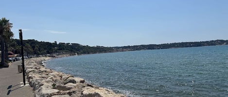 A coastal road with a rocky breakwater, clear skies, and a calm sea.
