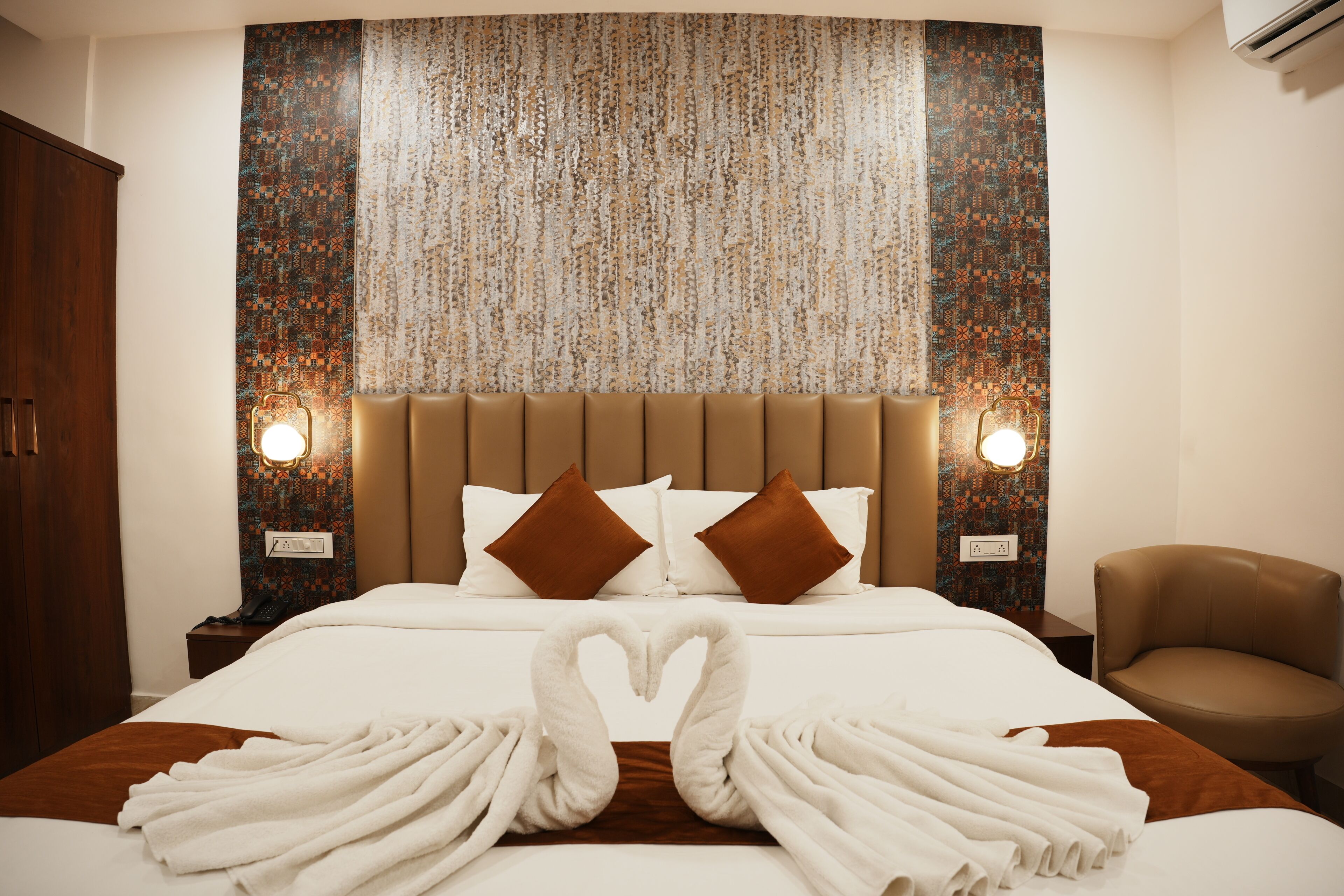 Habitación de hotel con una cama grande, dos almohadas, cabecera, lámparas de noche, una silla y una pared con textura.