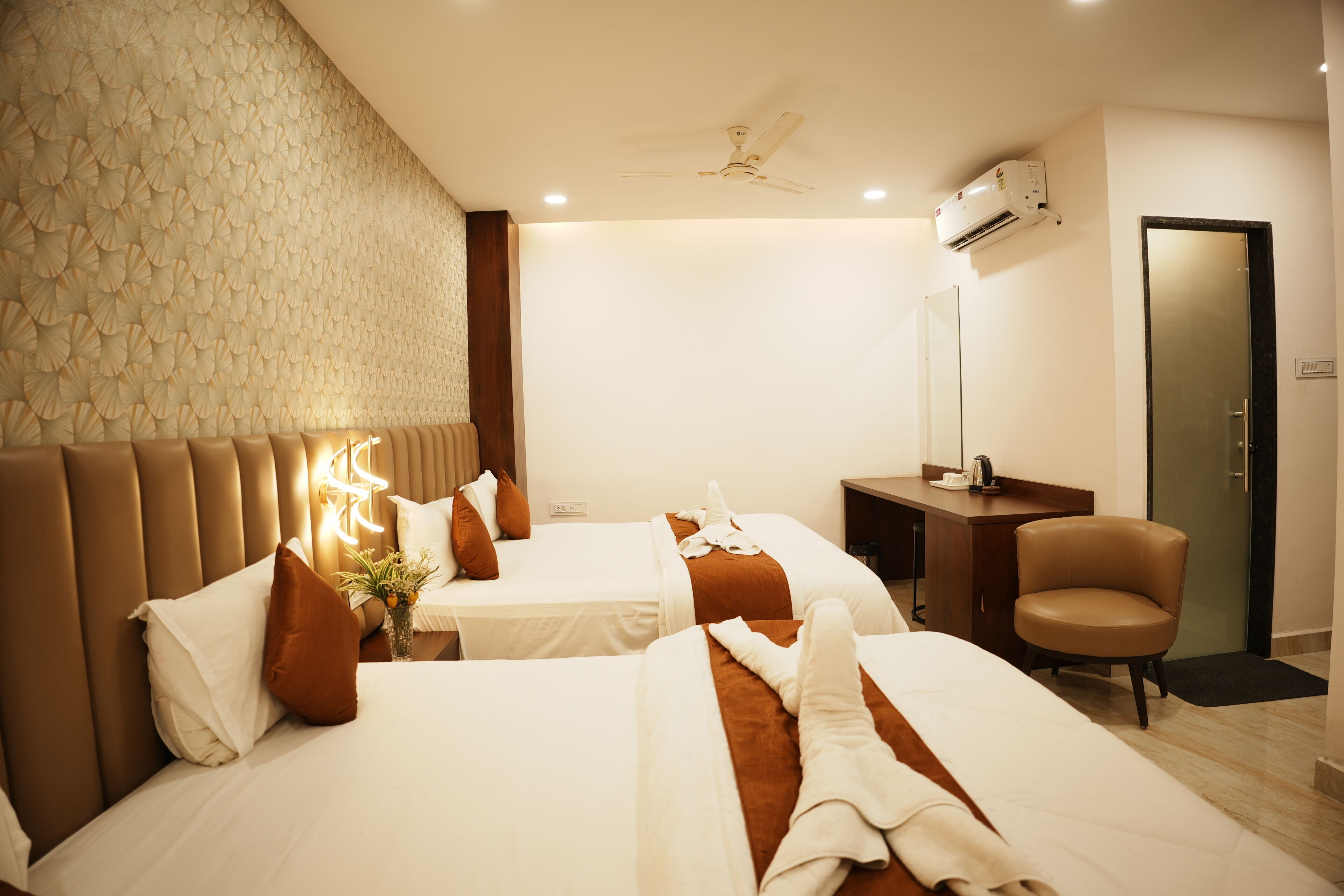 Ein Hotelzimmer mit zwei Betten, einem Schreibtisch, einem Stuhl, einem Deckenventilator und einer Klimaanlage.