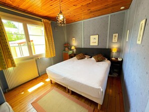 A bedroom with a wooden ceiling, a bed with white bedding, a nightstand with a lamp, and a window with curtains. - Charming lodge in the heart of Touraine (Montlouis-sur-Loire)