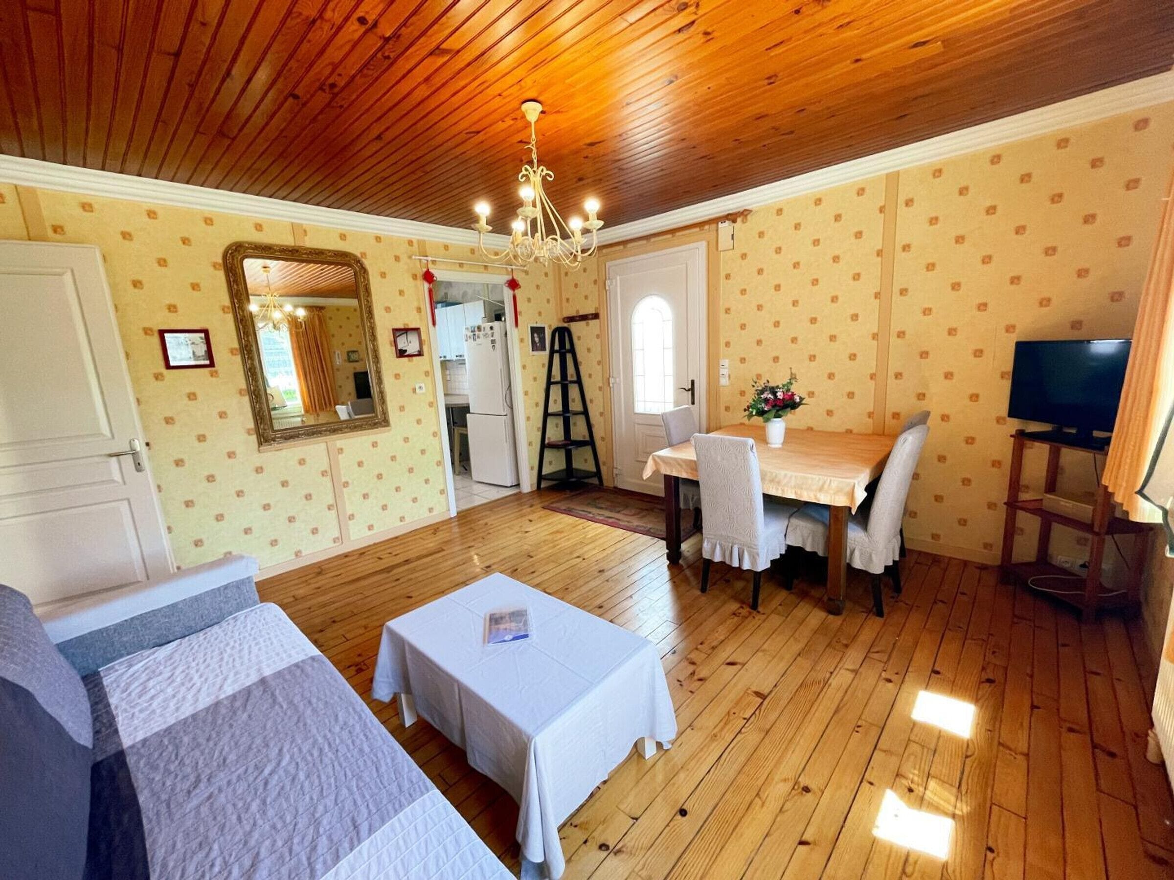 A cozy room with a wooden ceiling, a dining table with chairs, a television, and a bed with a white cover.