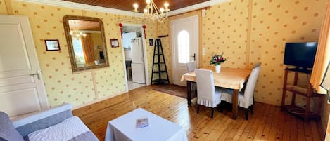 A cozy room with a wooden ceiling, a dining table with chairs, a television, and a bed with a white cover.