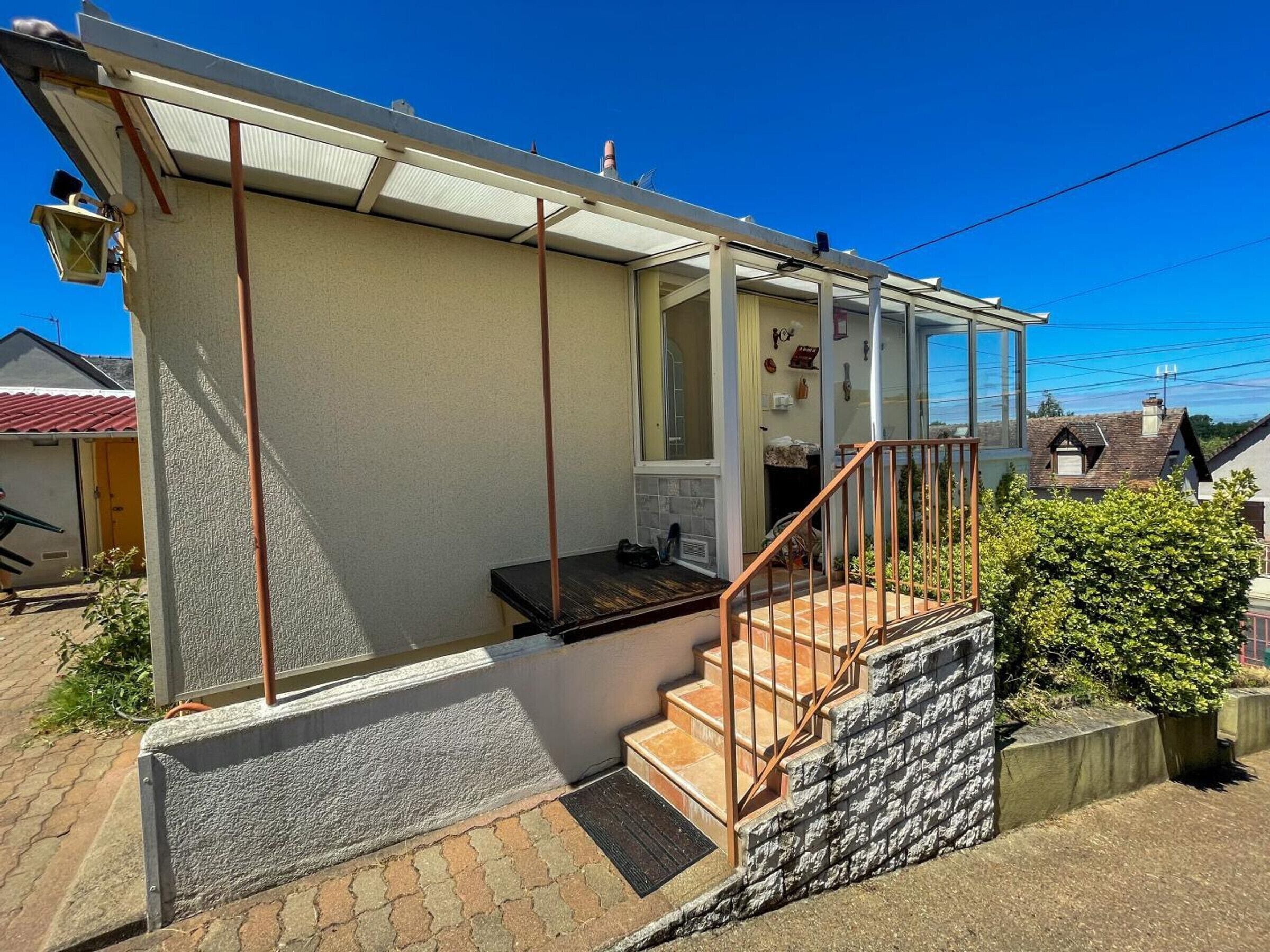 A residential building with a covered porch, a staircase leading to the entrance, and a small garden area.