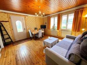 A cozy room with a wooden ceiling, a dining table with chairs, a sofa, a TV, and a window with curtains. - Charming lodge in the heart of Touraine (Montlouis-sur-Loire)