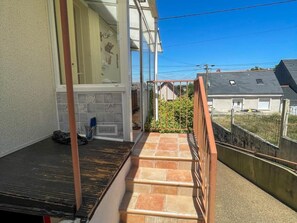 Ein Wohnhaus mit einer Treppe, die zu einem überdachten Außenbereich führt, einer gefliesten Wand und Blick auf Nachbarhäuser.