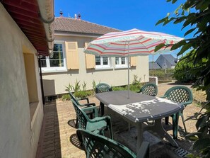 A patio with a table and chairs, an umbrella, and a house in the background. - Charming lodge in the heart of Touraine (Montlouis-sur-Loire)