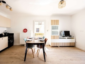 Una cocina moderna con lavadora, comedor con mesa preparada para cuatro personas y televisor sobre un mueble.