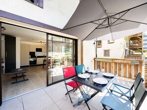 Un patio exterior con una mesa lista para comer, una puerta corrediza de vidrio que da a una cocina y una terraza de madera.