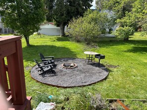 Un jardin avec un foyer circulaire, deux fauteuils Adirondack et une petite table.