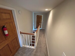 A hallway with a wooden door, a fire extinguisher, a white railing, and a carpeted floor.