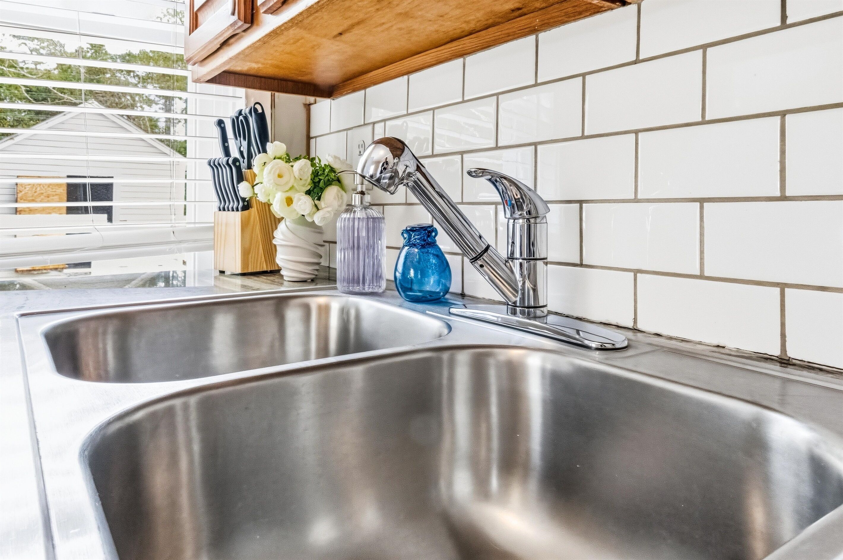 A stainless steel kitchen sink with a modern faucet, a wooden ceiling, and white tiled backsplash.