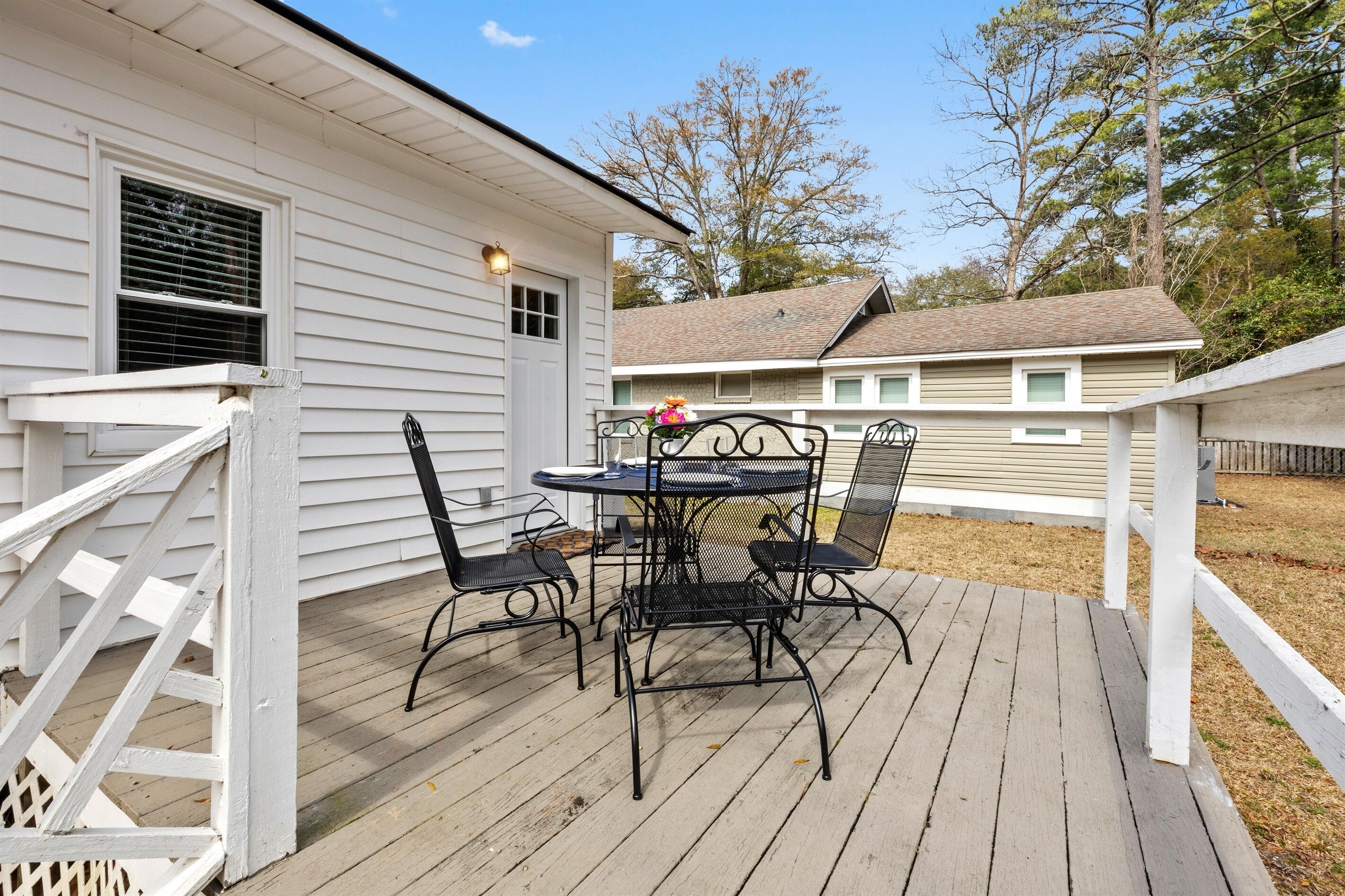Une terrasse en bois avec une table et des chaises en métal, une clôture blanche et une maison en arrière-plan.