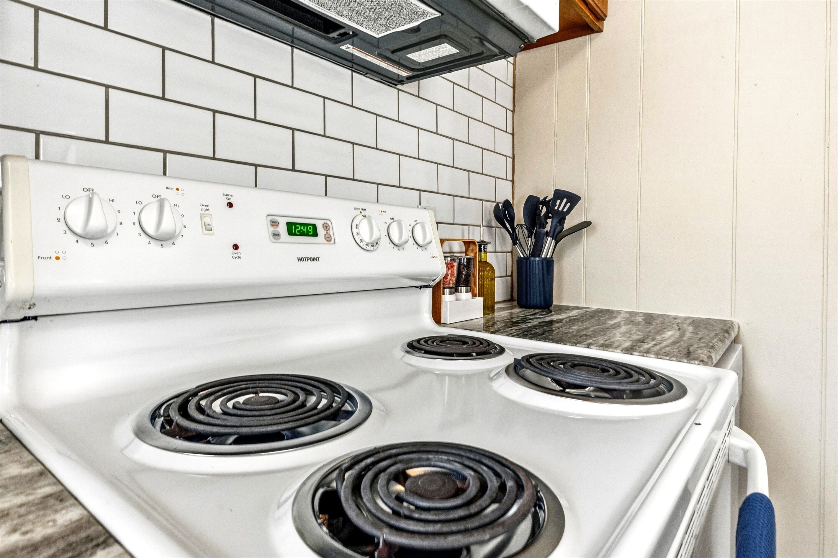 A kitchen with a white stove, four burners, and a digital clock displaying 12:49.