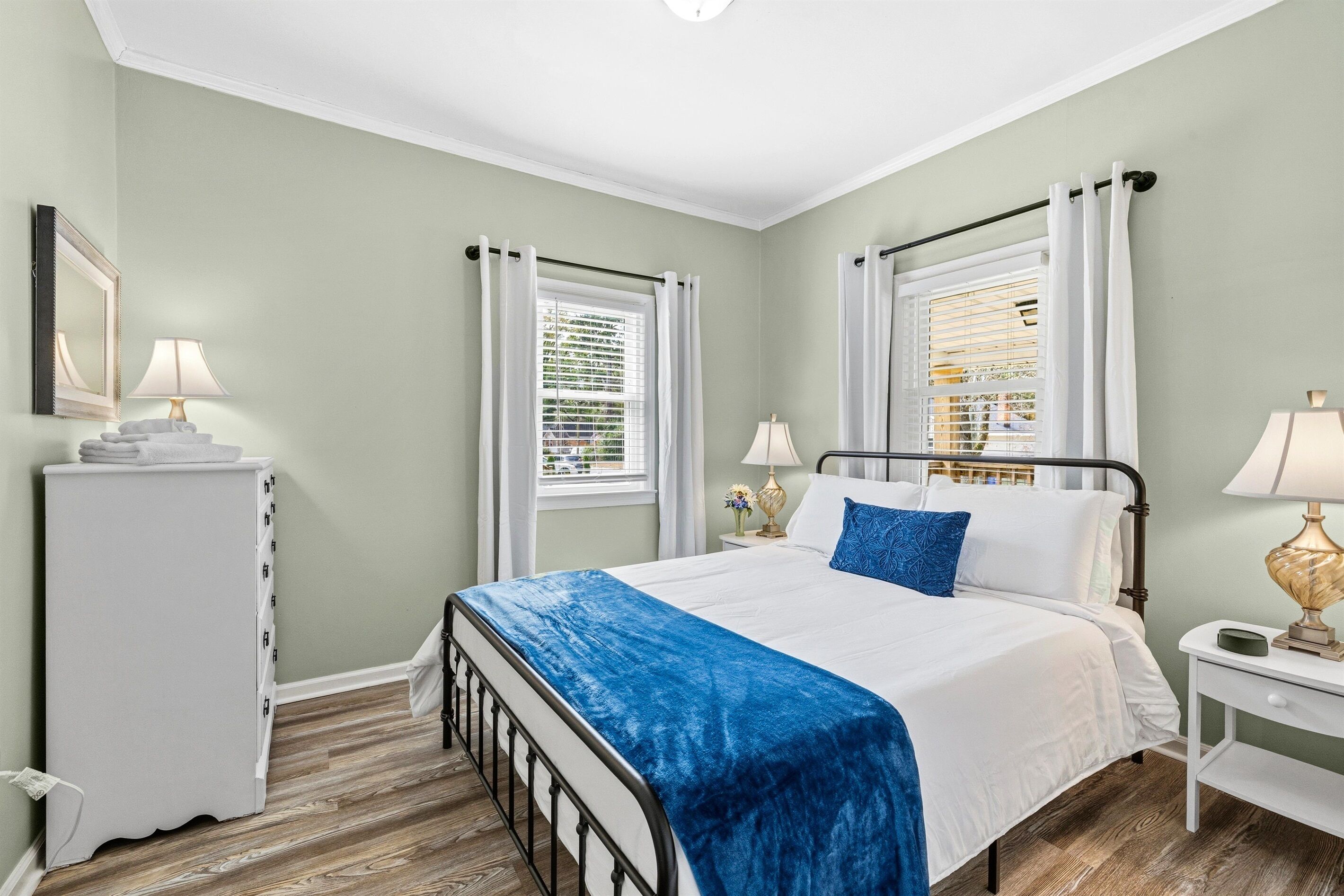 A bedroom with a bed, two bedside tables, a nightstand, a dresser, and a window with curtains.
