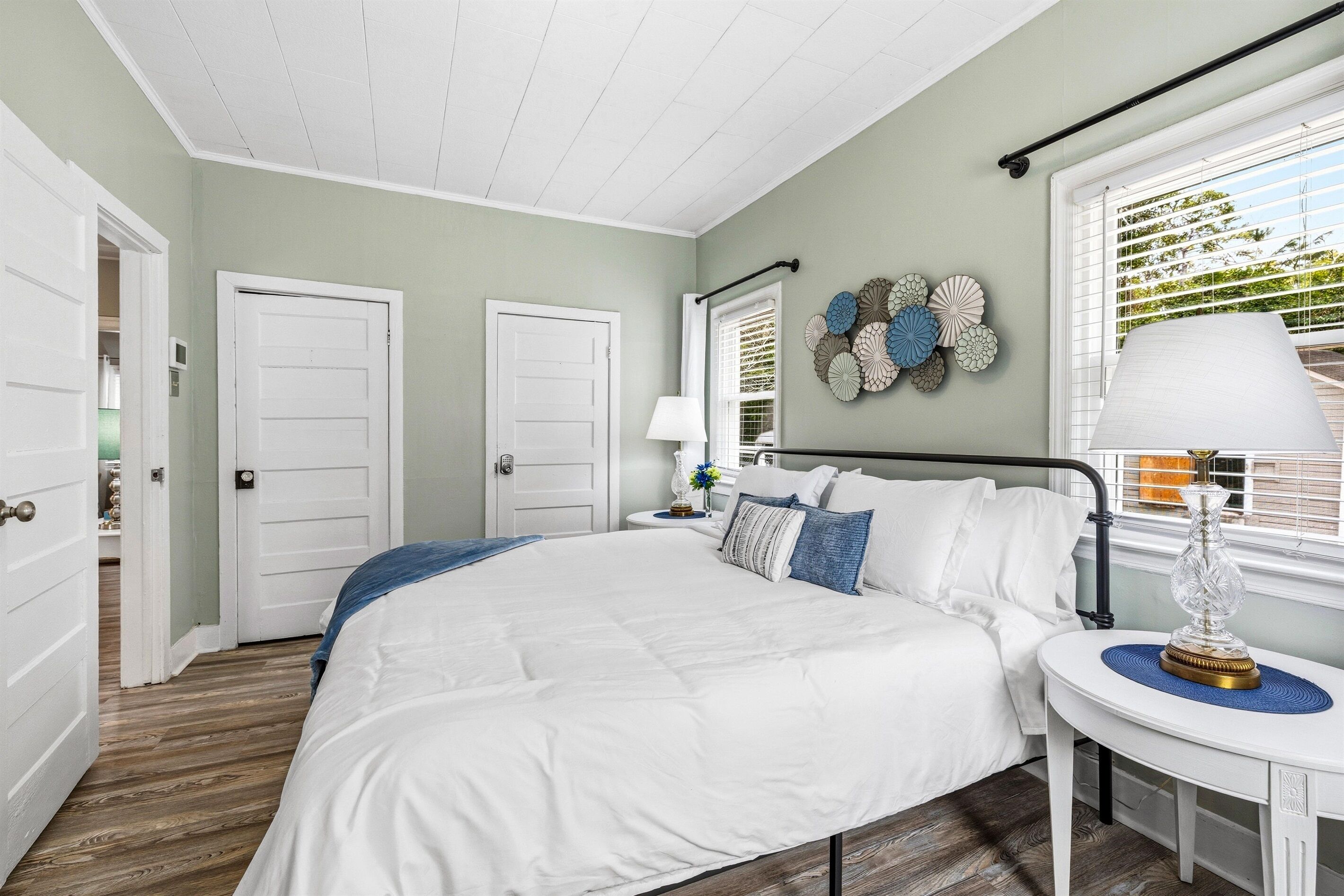 Une chambre à coucher avec un grand lit, deux portes, une table de chevet avec une lampe et un élément décoratif mural.