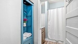 A bathroom with a shower curtain, a towel rack, and a blue cabinet with a vase of flowers.