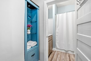 A bathroom with a shower curtain, a towel rack, and a blue cabinet with a vase of flowers.