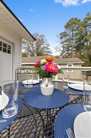 A patio table set with blue placemats, clear glassware, and a white pitcher with a floral arrangement.