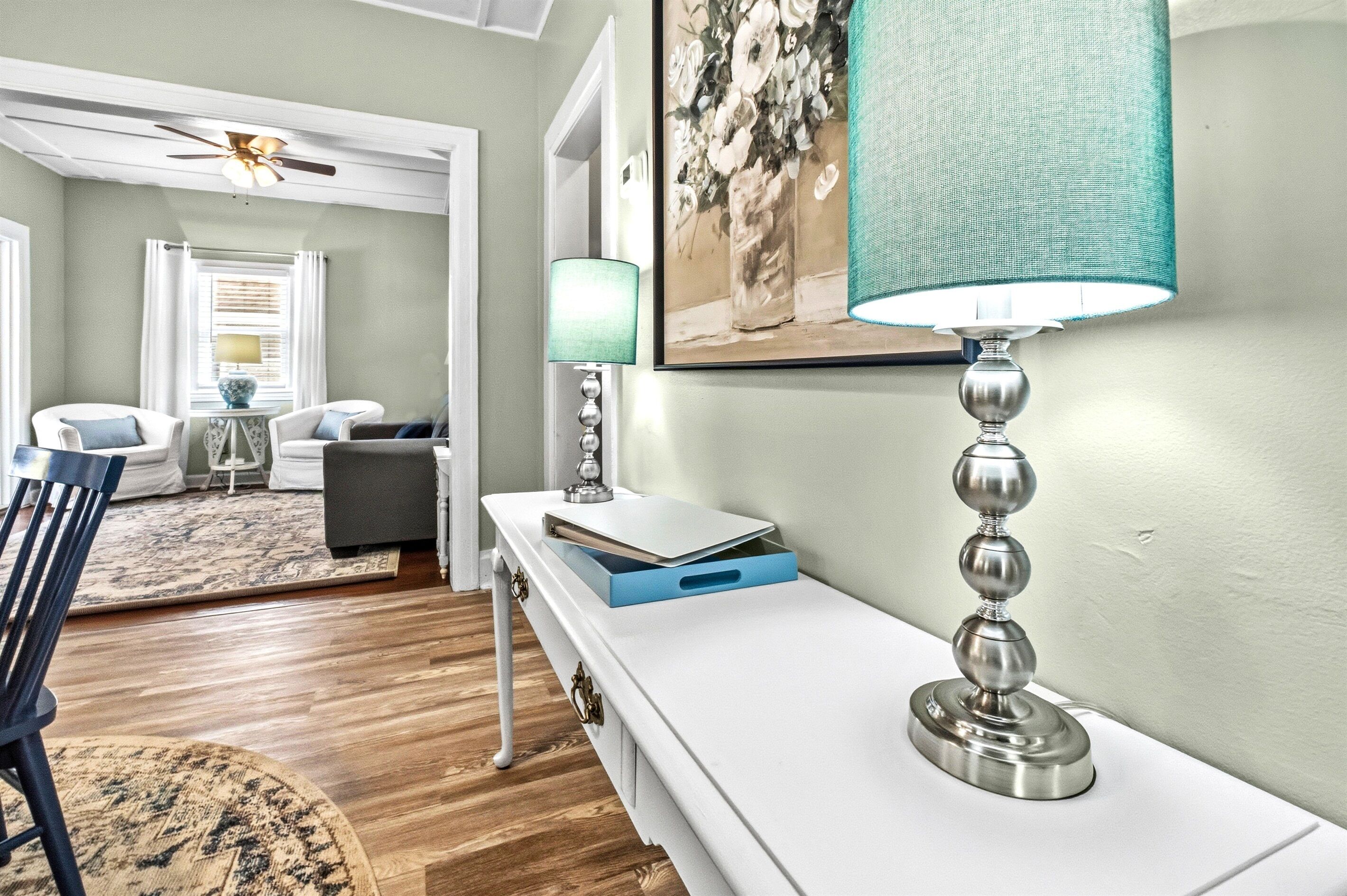 A room with a white desk, a lamp, a chair, a rug, and a ceiling fan.