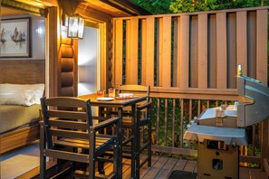 A wooden deck with a grill, a table with chairs, and a bed with a headboard. - Evergreen Retreat: Fresh Remodel, Near The Island (Pigeon Forge)