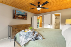 A bedroom with a bed, a dresser, a ceiling fan, a painting, and a door leading to another room. - Evergreen Retreat: Fresh Remodel, Near The Island (Pigeon Forge)