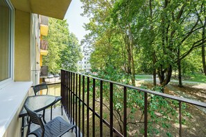 Un balcone con tavolo e sedie, affaccia su un parco con alberi e un edificio sullo sfondo.