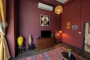 A room with a wooden cabinet, a television, a statue, a vase, and a patterned rug. - Inpeng View Hotel (Vientiane)