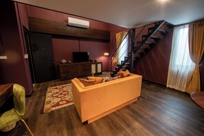 A living room with a sofa, a television, a staircase, and a wall-mounted air conditioner. - Inpeng View Hotel (Vientiane)