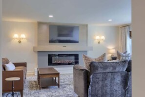 A living room with a fireplace, a flat-screen TV mounted above it, and two wall-mounted lamps.