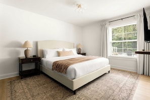 A bedroom with a bed, nightstands, a rug, a window with blinds, and a ceiling light.