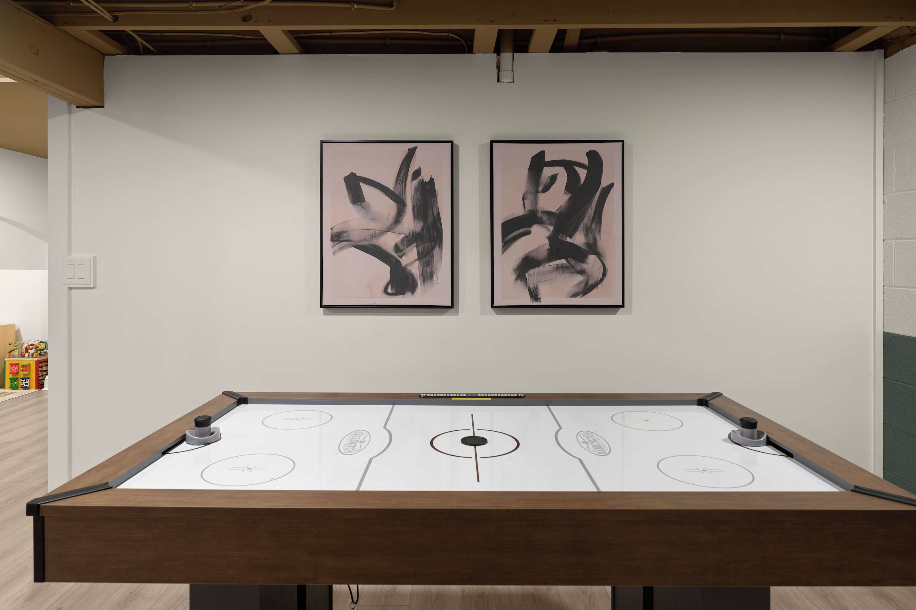 Une table de billard avec un cadre en bois et un plateau de jeu blanc, encadrée de deux peintures abstraites noires sur un mur blanc.