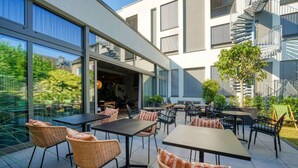 An outdoor patio area with tables and chairs, a staircase, and a building with large windows and balconies.
