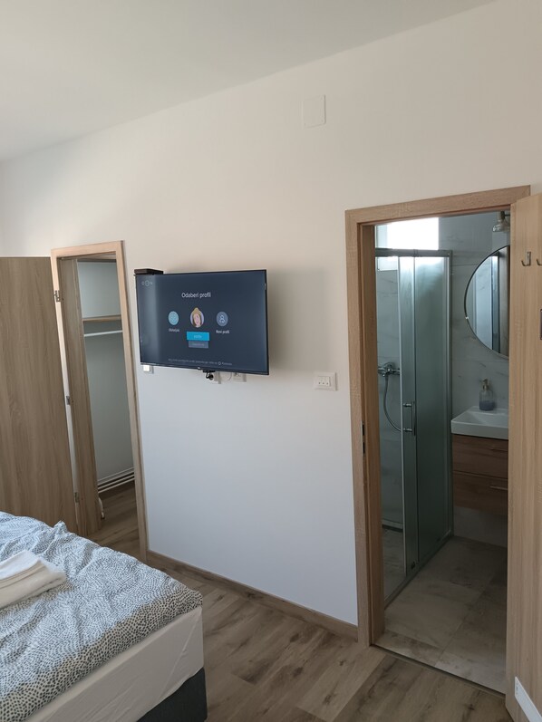 A bedroom with a bed, a TV mounted on the wall, and a bathroom with a glass shower door.