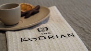 A close-up of a napkin with the text 'THE KODRIAN' and a cup and pastry on a plate. - Cozy Queen, The Kodrian (Athens)