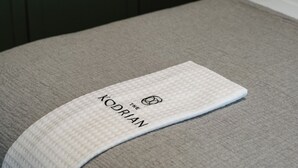 A pillow with a white cover featuring the text 'The Kodrian' and a logo. - Cozy Queen, The Kodrian (Athens)