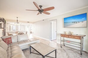 Ein geräumiges Wohnzimmer mit Deckenventilator, einem großen Fenster mit Blick auf den Strand, einem Essbereich mit Korbmöbeln und einer Küche im modernen Design.