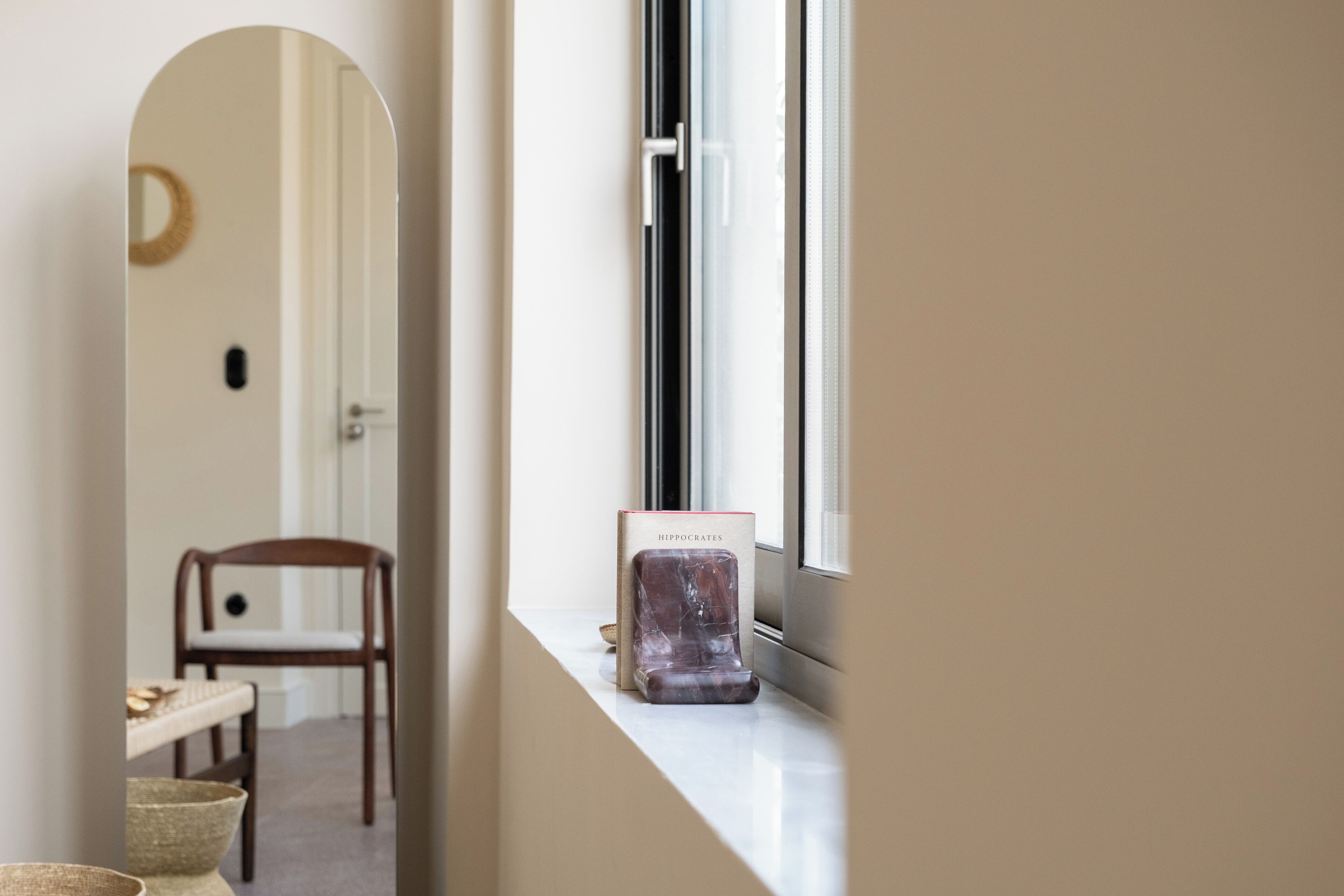 A hallway with a window sill, a mirror, a chair, and a small table with a bowl.