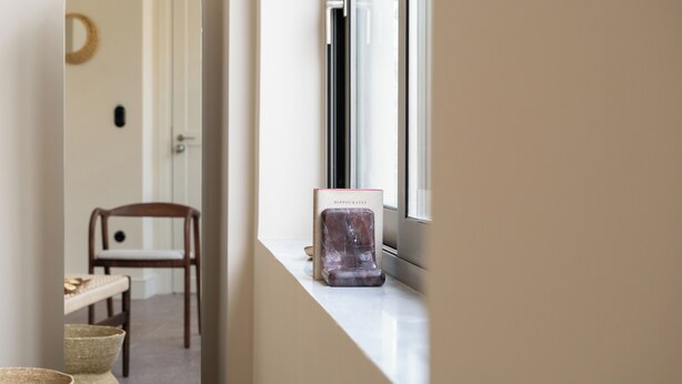 Ein Flur mit Fensterbank, Spiegel, Stuhl und einem kleinen Tisch mit einer Schale.