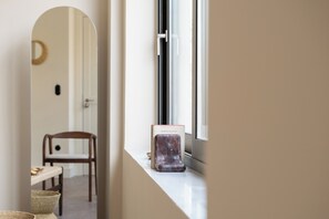 Un corridoio con un davanzale, uno specchio, una sedia e un tavolino con una ciotola.