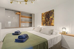 A bedroom with a bed, pillows, a green blanket, a window with wooden blinds, a wall-mounted picture, and a bedside lamp. - Jazmín 1A – Sea View Holiday Home in Capistrano Village (Nerja)