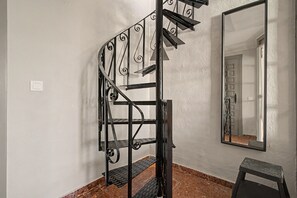 A spiral staircase with a metal railing, a mirror on the wall, and a small stool. - Jazmín 1A – Sea View Holiday Home in Capistrano Village (Nerja)