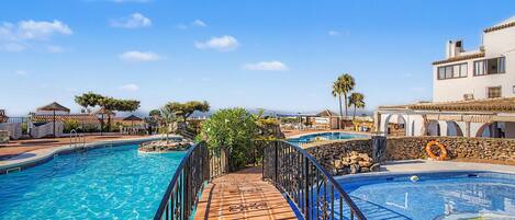 A resort with multiple swimming pools, a covered walkway, and a view of the surrounding landscape.