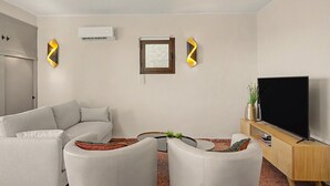 Un salon moderne avec un canapé, deux fauteuils, un téléviseur et une petite table agrémentée de plantes.