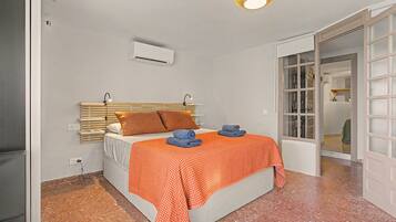 A bedroom with a bed, a wall-mounted air conditioner, a window with a view, and a door leading to another room.