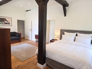 Un dormitorio con una cama grande, una silla de madera, una mesita y un cuadro en la pared.