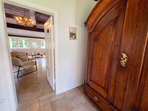Una habitación con un armario de madera, una lámpara de araña y vistas a otra habitación con un sofá y una mesa.