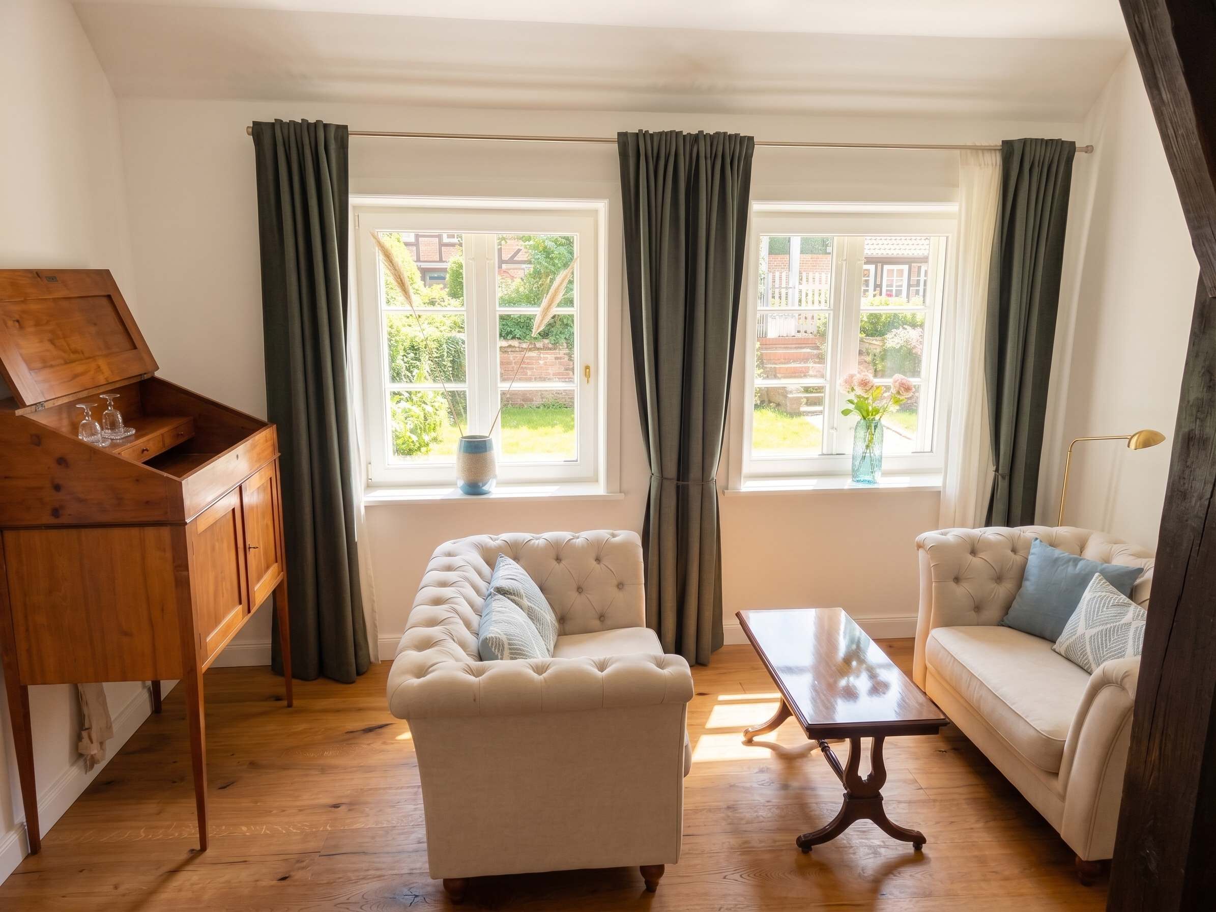 A living room with a wooden piano, two sofas, a coffee table, and a view of a garden through large windows.