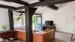 A modern living room with a sofa, a coffee table with fruit, a TV, and a door leading outside. - FH Luhe-Hof - Historisches Reetdachanwesen (Winsen (Luhe))